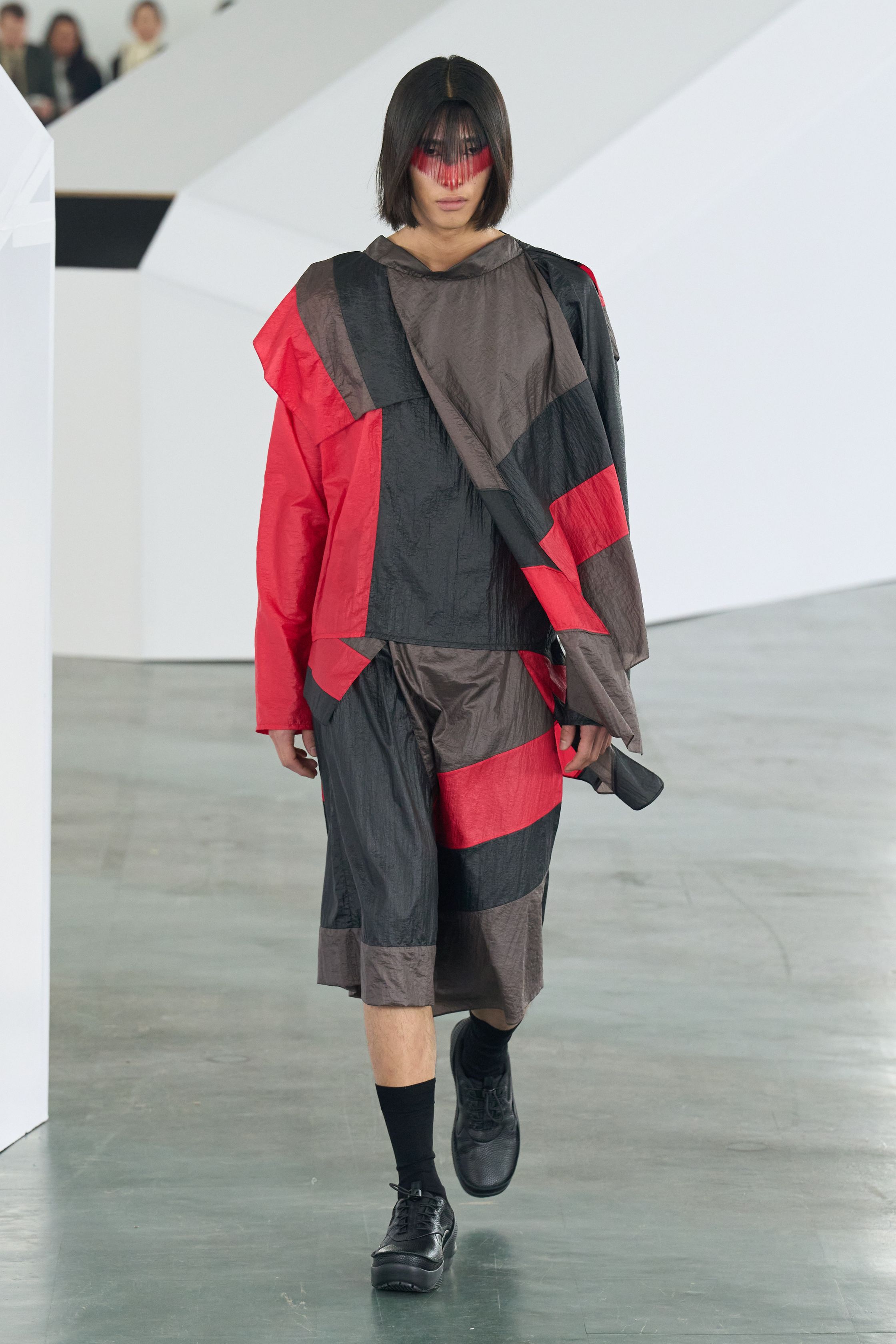 Kiko Kostadinov 26FW 继续深化其结构语言，以功能主义为表象，内核却极度诗性。不对称剪裁、分割式廓形与工业面料共同构建出一种“行走中的系统服装”。红黑配色与面部遮挡强化仪式感，使服装看似冷静却暗含张力。Kiko 的设计始终拒绝讨好市场，而是为思想型穿着者构建独立审美秩序-顽石频道趋势研究